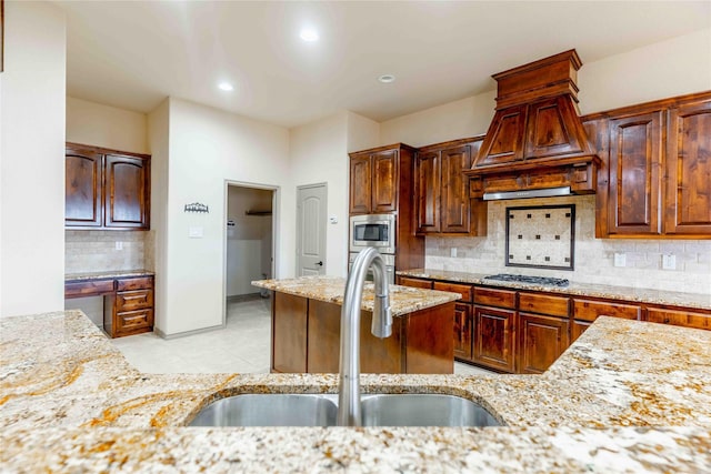 kitchen featuring light stone countertops, custom exhaust hood, stainless steel appliances, tasteful backsplash, and sink