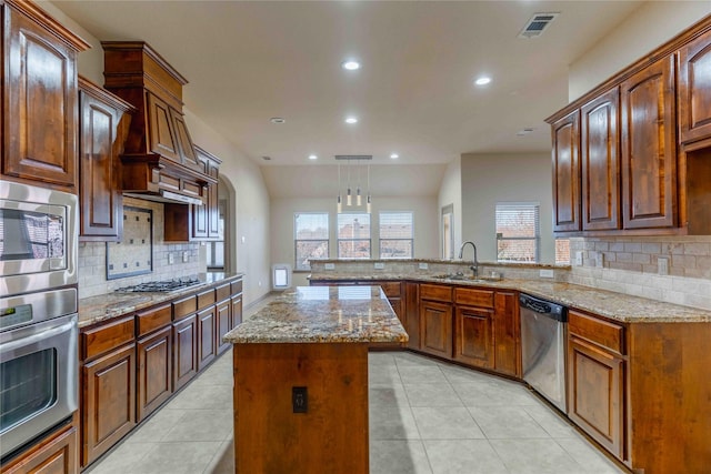 kitchen featuring appliances with stainless steel finishes, sink, decorative light fixtures, light stone countertops, and a kitchen island