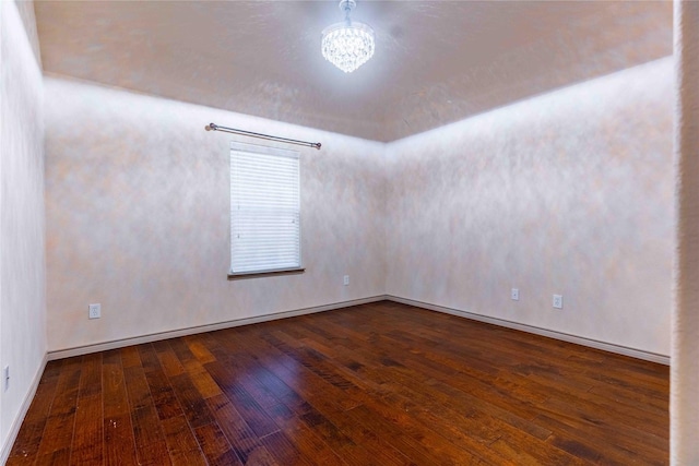 unfurnished room with a notable chandelier and dark hardwood / wood-style flooring