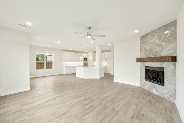 unfurnished living room with a premium fireplace, a ceiling fan, baseboards, light wood-type flooring, and visible vents