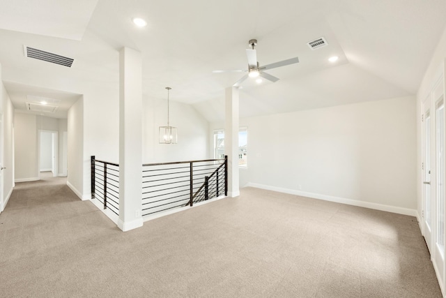 carpeted empty room featuring ceiling fan with notable chandelier, visible vents, attic access, and lofted ceiling
