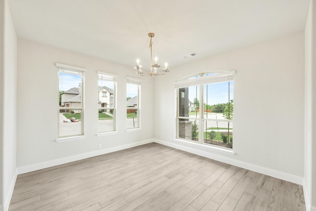 unfurnished dining area featuring a healthy amount of sunlight, baseboards, light wood-style flooring, and a notable chandelier