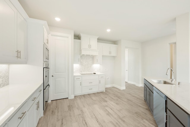 kitchen featuring white cabinets, a sink, backsplash, light wood-type flooring, and stainless steel dishwasher