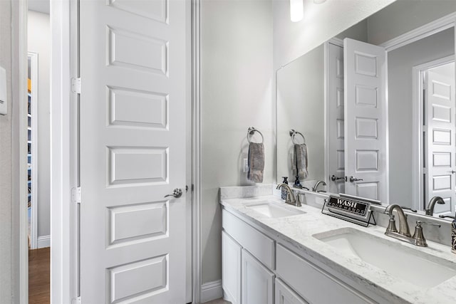 bathroom featuring wood finished floors, a sink, baseboards, and double vanity