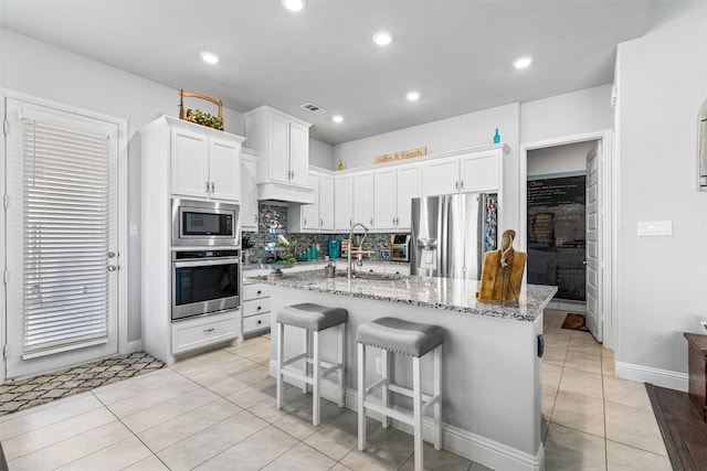 kitchen featuring appliances with stainless steel finishes, white cabinetry, light tile patterned flooring, a kitchen island with sink, and a breakfast bar area