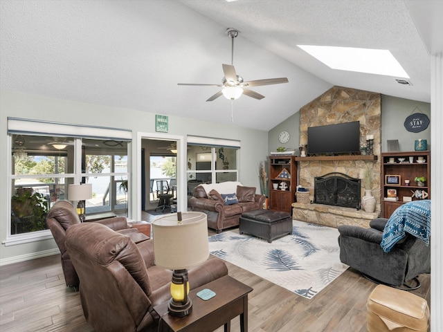 living room with hardwood / wood-style flooring, ceiling fan, a fireplace, and vaulted ceiling with skylight