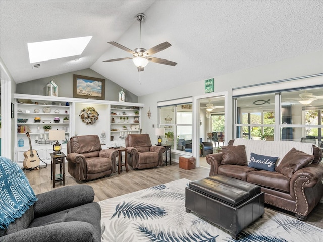 living room with wood-type flooring, a textured ceiling, ceiling fan, and lofted ceiling with skylight