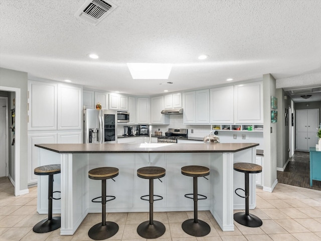 kitchen with white cabinets, a breakfast bar area, light tile patterned floors, and stainless steel appliances