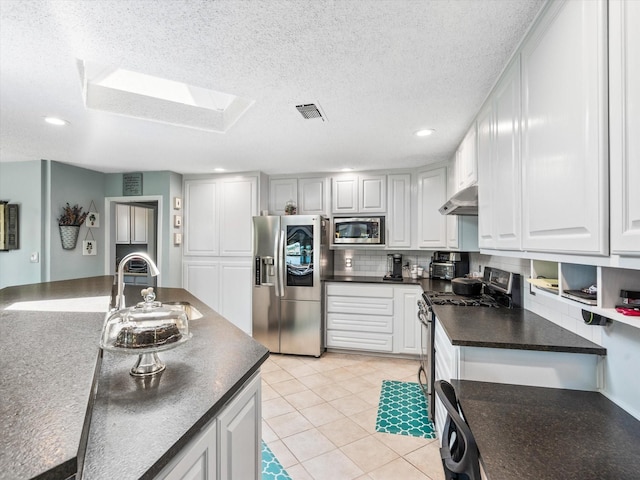 kitchen with white cabinets, a textured ceiling, light tile patterned floors, and appliances with stainless steel finishes