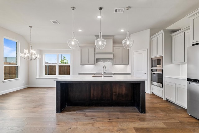 kitchen featuring wood-type flooring, sink, decorative light fixtures, stainless steel appliances, and a center island with sink