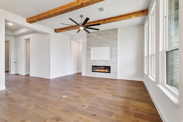 unfurnished living room featuring wood-type flooring, a tiled fireplace, vaulted ceiling with beams, and ceiling fan