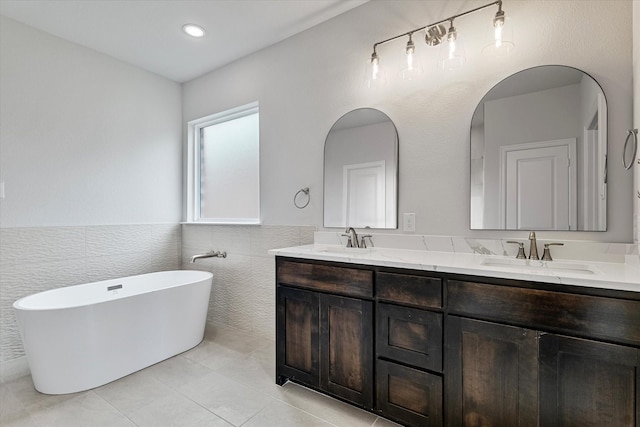 bathroom with tile walls, a tub to relax in, vanity, and tile patterned flooring