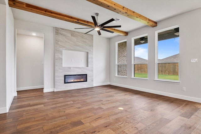 unfurnished living room featuring hardwood / wood-style flooring, a tile fireplace, and beam ceiling