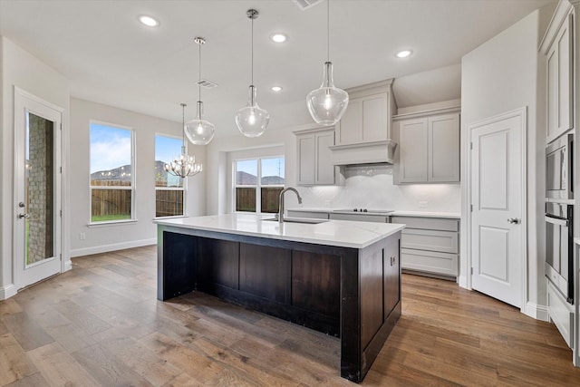 kitchen featuring hardwood / wood-style floors, appliances with stainless steel finishes, decorative light fixtures, sink, and a center island with sink