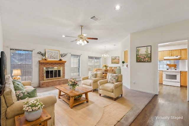 living room with a healthy amount of sunlight, a brick fireplace, ceiling fan with notable chandelier, and light hardwood / wood-style flooring