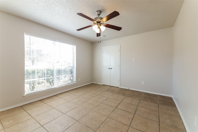 empty room featuring a textured ceiling, light tile patterned floors, and ceiling fan