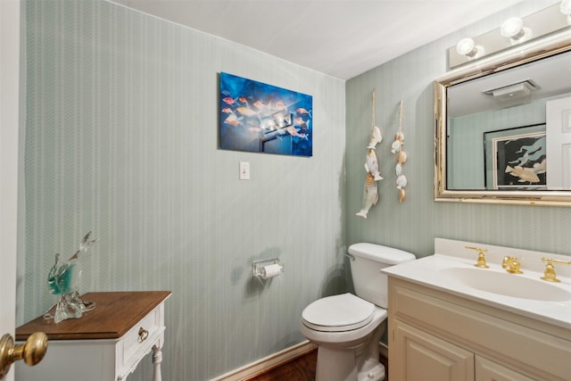 half bath featuring vanity, toilet, and wallpapered walls