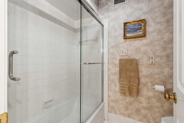 bathroom with toilet, shower / bath combination with glass door, and visible vents