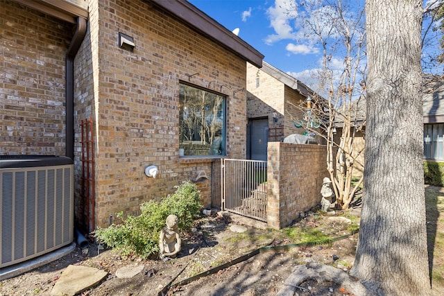 view of side of home with central AC, brick siding, and fence