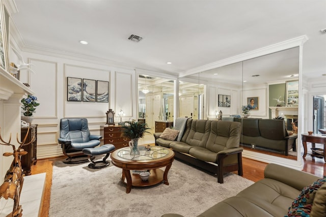 living room featuring crown molding, a fireplace, light wood finished floors, visible vents, and a decorative wall