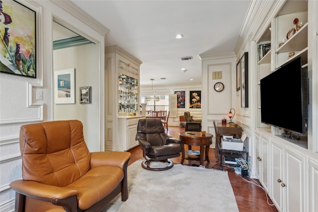 living area with dark wood-style flooring, crown molding, recessed lighting, visible vents, and a decorative wall