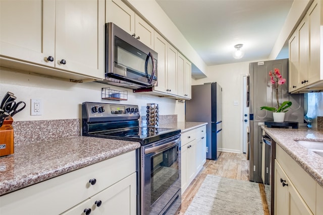 kitchen featuring light stone countertops, appliances with stainless steel finishes, and light wood-type flooring