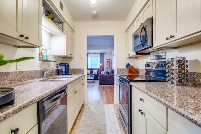 kitchen featuring sink, light stone counters, light wood-type flooring, and appliances with stainless steel finishes