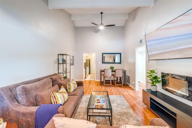 living room featuring ceiling fan, beamed ceiling, light hardwood / wood-style flooring, and high vaulted ceiling