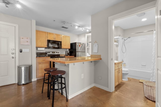 kitchen with a kitchen breakfast bar, light brown cabinets, kitchen peninsula, concrete floors, and stainless steel appliances