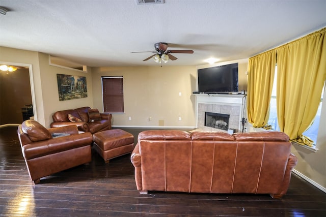 living room with ceiling fan, dark wood-type flooring, a textured ceiling, and a tiled fireplace