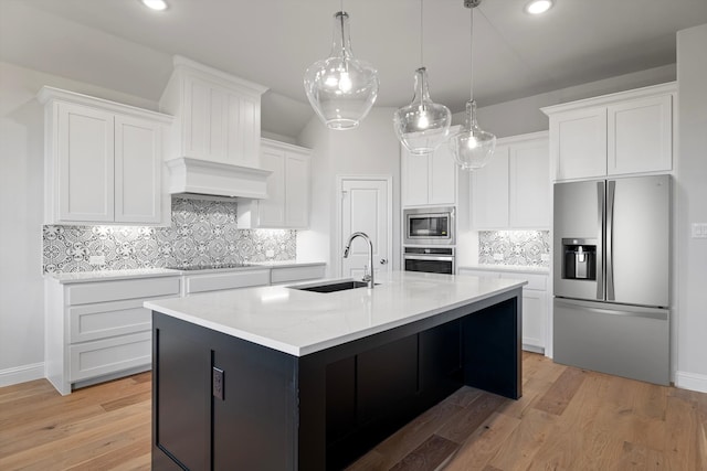 kitchen with white cabinets, stainless steel appliances, sink, backsplash, and a center island with sink