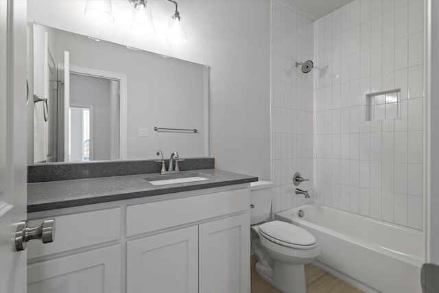 full bathroom with vanity, hardwood / wood-style flooring, tiled shower / bath, and toilet