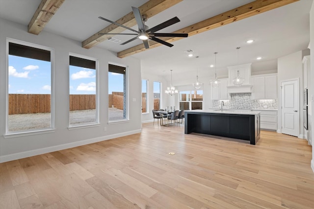 kitchen featuring beamed ceiling, decorative backsplash, white cabinets, pendant lighting, and a center island with sink