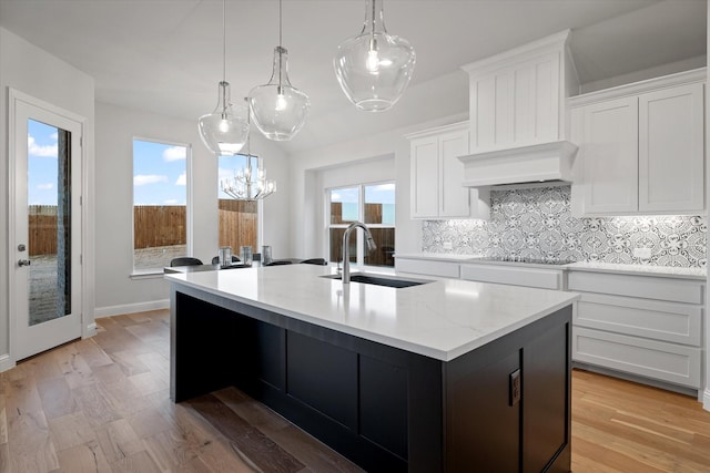 kitchen with white cabinetry, sink, hanging light fixtures, a kitchen island with sink, and light wood-type flooring