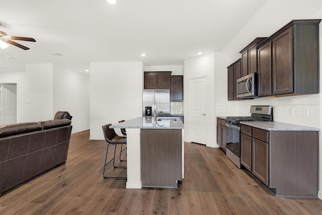 kitchen with light stone countertops, appliances with stainless steel finishes, dark hardwood / wood-style flooring, an island with sink, and sink