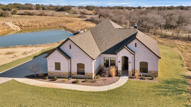 french country style house with brick siding, a water view, a front lawn, and roof with shingles