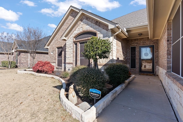 property entrance featuring stone siding, brick siding, and roof with shingles