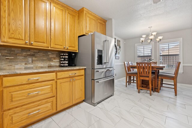 kitchen with high quality fridge, a textured ceiling, decorative backsplash, a chandelier, and light stone counters