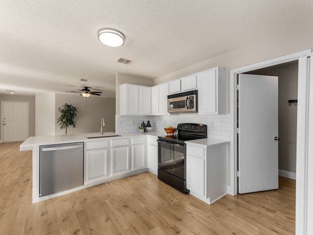 kitchen with kitchen peninsula, appliances with stainless steel finishes, sink, white cabinets, and decorative backsplash