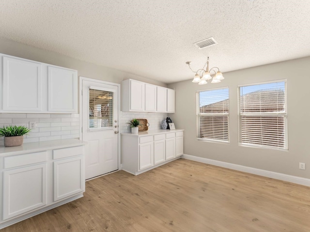 kitchen featuring white cabinets, hanging light fixtures, light hardwood / wood-style flooring, and decorative backsplash