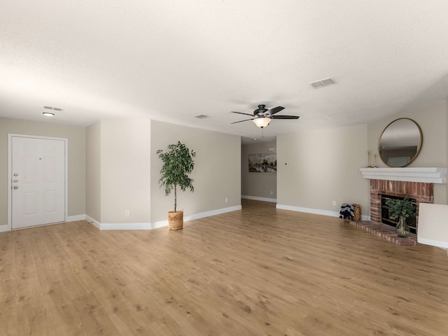 unfurnished living room featuring a brick fireplace, light hardwood / wood-style floors, a textured ceiling, and ceiling fan