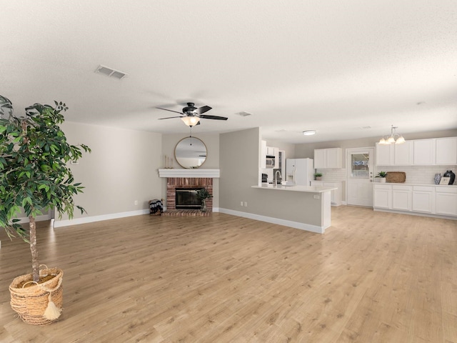 unfurnished living room featuring a brick fireplace, sink, and light wood-type flooring