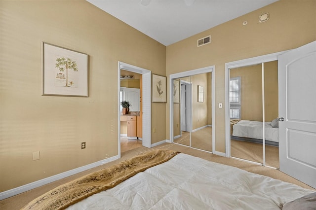 bedroom with ensuite bathroom, light carpet, and multiple closets