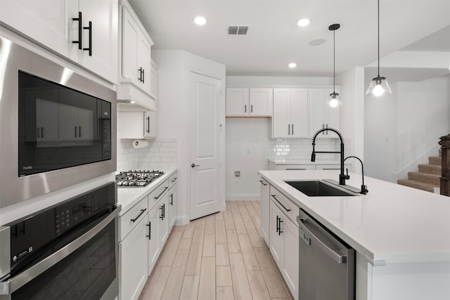 kitchen with appliances with stainless steel finishes, pendant lighting, sink, white cabinets, and a center island with sink