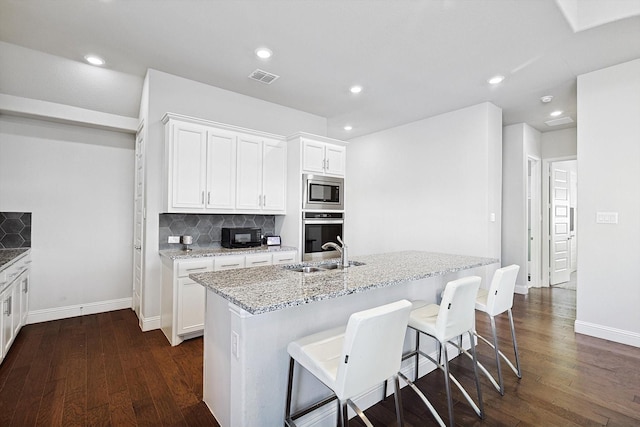 kitchen featuring appliances with stainless steel finishes, white cabinetry, decorative backsplash, sink, and a center island with sink