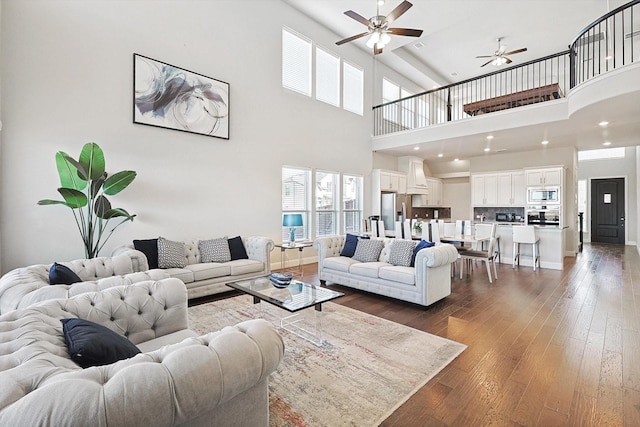 living room with a towering ceiling, ceiling fan, and dark hardwood / wood-style flooring