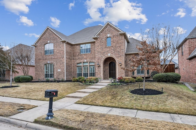 traditional-style house with brick siding, a shingled roof, and a front yard