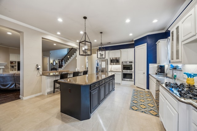 kitchen with a center island, appliances with stainless steel finishes, white cabinetry, dark stone countertops, and decorative light fixtures