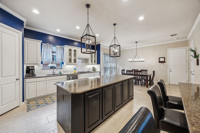 kitchen featuring hanging light fixtures, sink, white cabinetry, a center island, and dark stone countertops