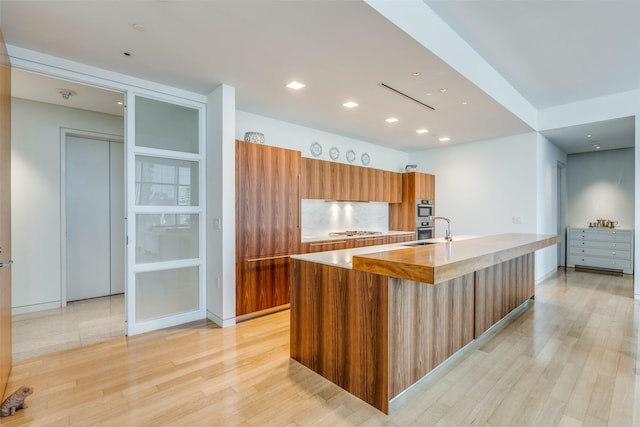 kitchen with sink, stainless steel gas cooktop, a kitchen island with sink, and light wood-type flooring